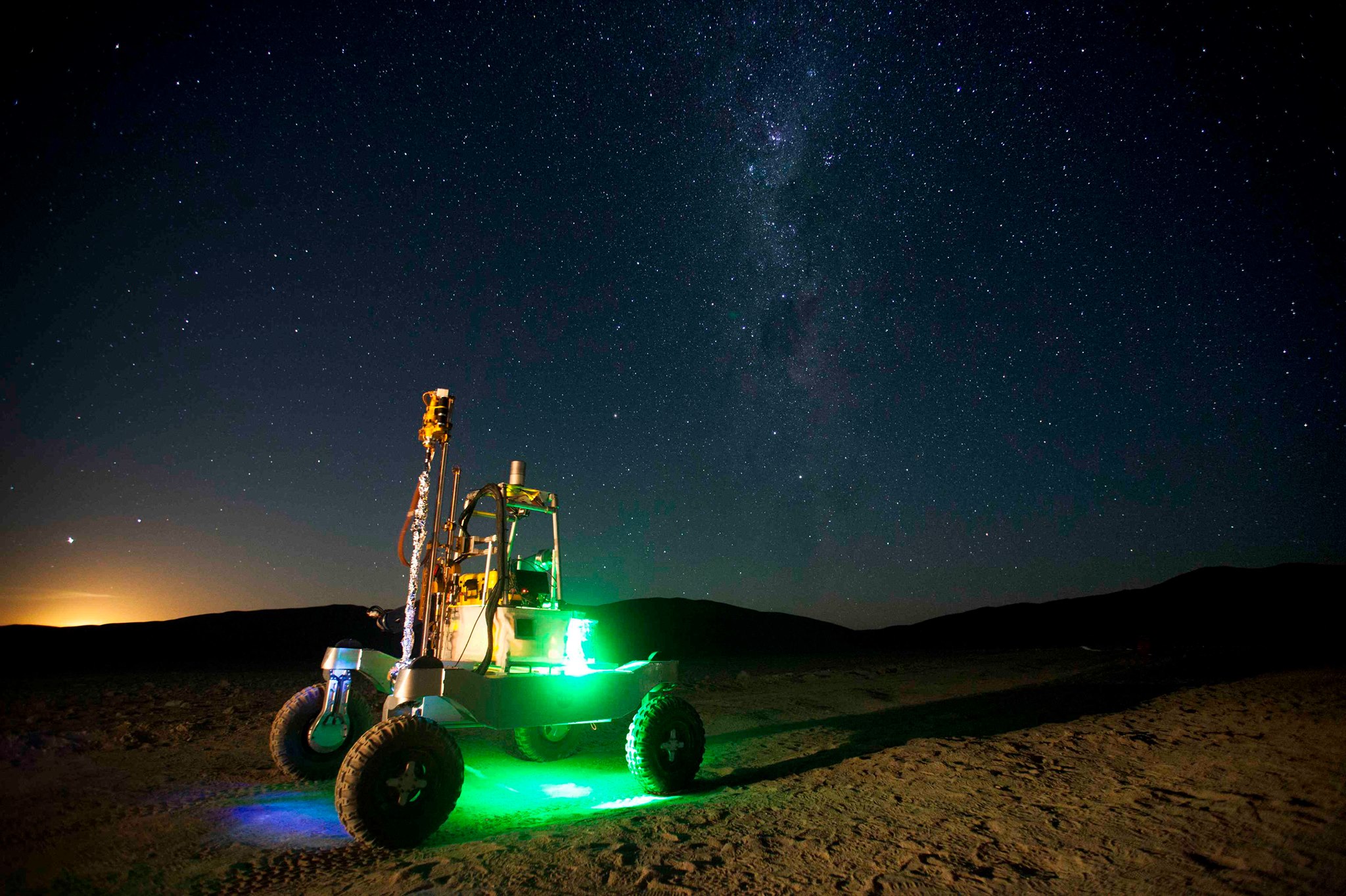Mars rover traversing plains while lit by the dawn, a small blue pilot light, and a green internally placed lightbulb.