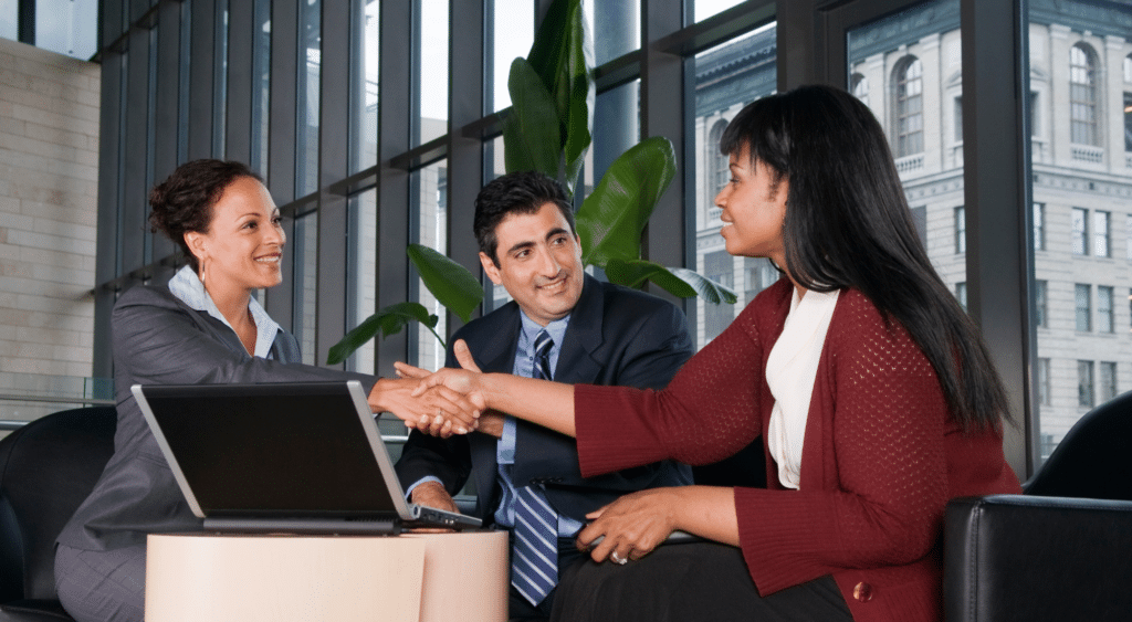Three professionals meeting and shaking hands in an office, symbolizing reconnecting with federal buyers.